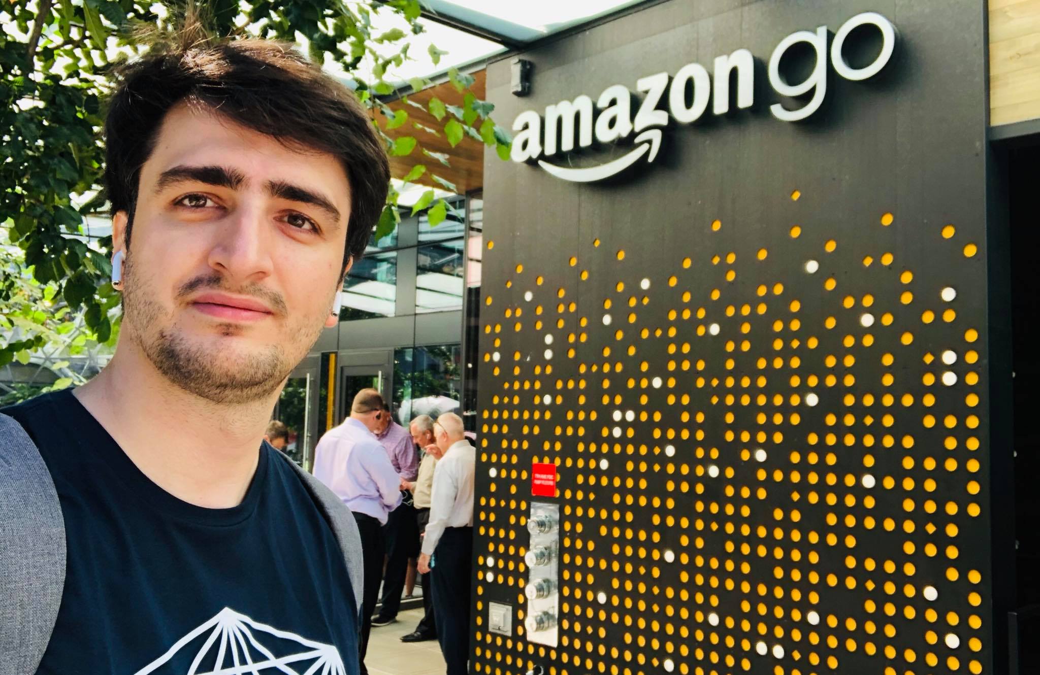 Me smiling for a selfie outside an Amazon Go store, next to the illuminated "amazon go" sign on the storefront wall.