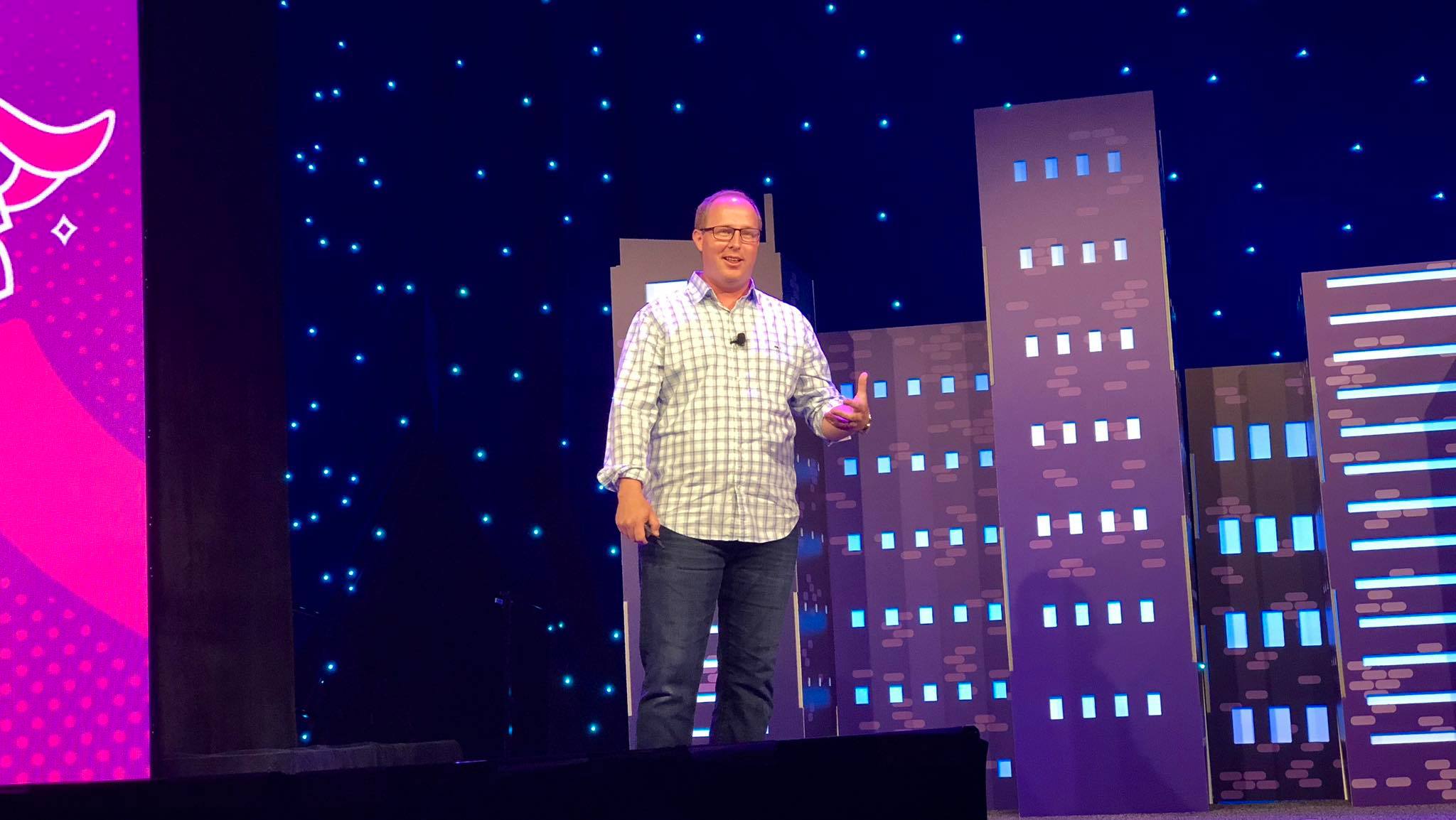 Russ Jones pausing on the MozCon stage, the Space Needle rendered in blue light on the skyline backdrop behind him.